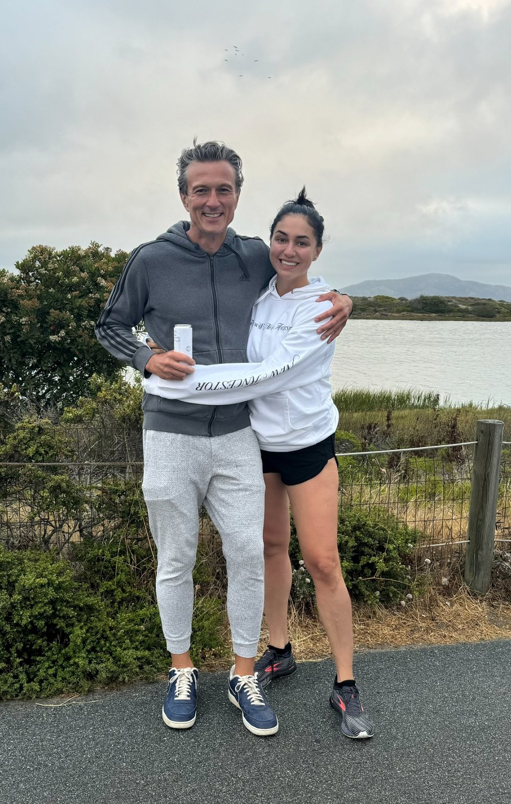The founders of MOON BOO SUN Farah and Maciej holding a can of MOON BOO SUN 100% organic coconut water and wearing branded hoodie, representing healthy hydration, active lifestyle, and premium coconut water brand